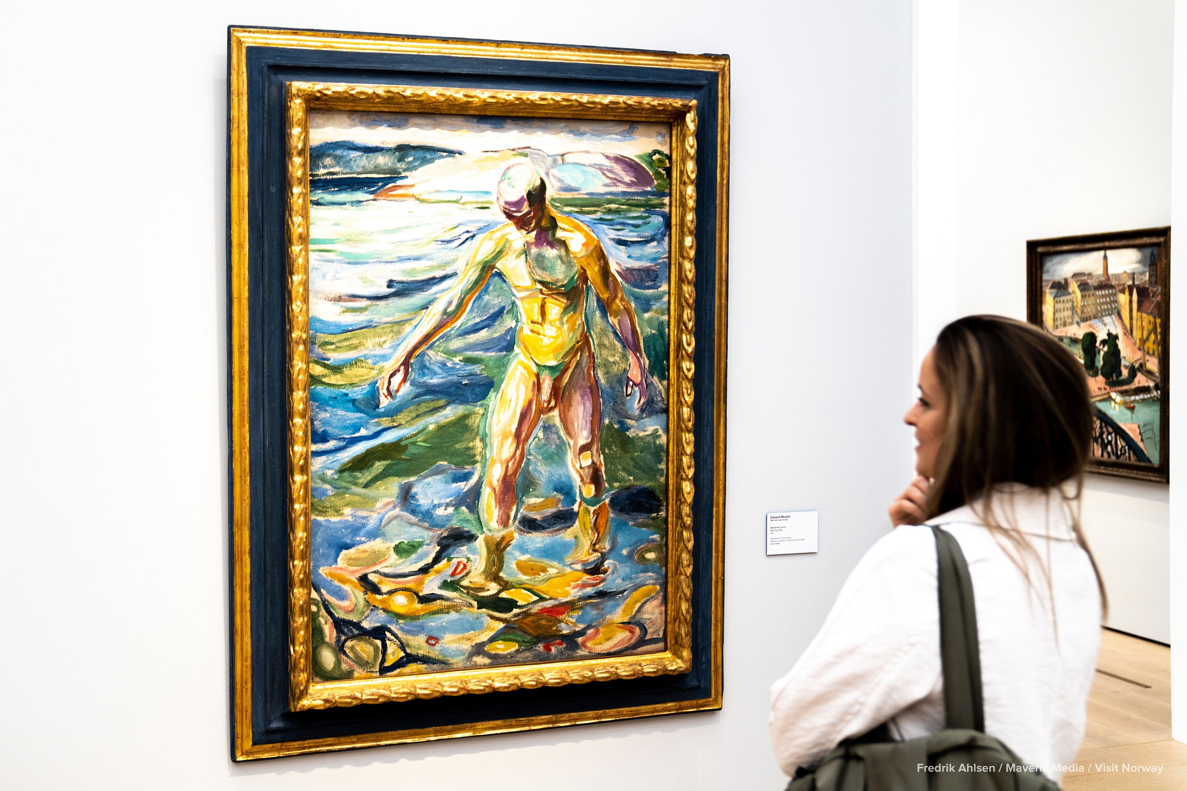 A woman observes a colorful framed painting of a figure standing in water.